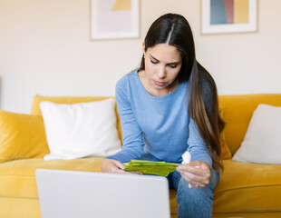 Young sick woman reading medication instructions while sitting on sofa at home. Telemedicine and medical lifestyle concept