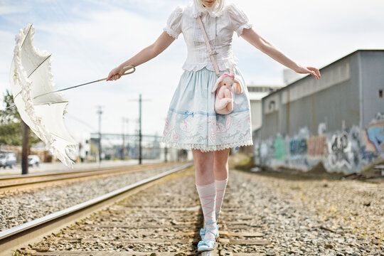 Portrait of a woman dressed as a little girl, walking along train tracks in Portland, Oregon.