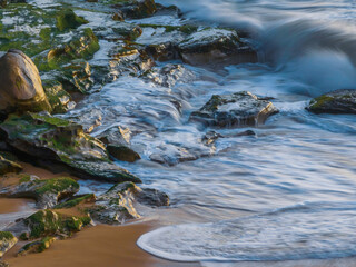 Sunrise at the seaside with waves breaking on the rocks