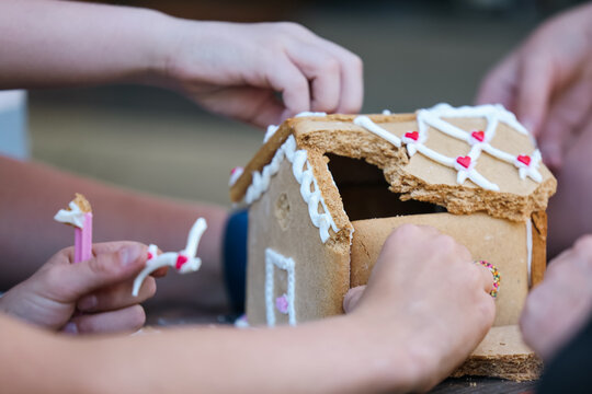 Children's Hands Pulling Apart Gingerbread House At Christmas Time