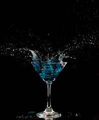 Blue Cocktail Glass with splashing water alcohol, Crystal Cocktail drink splatter splash in air and bubble from glass. Liquor Part freeze shot high speed over black background isolated