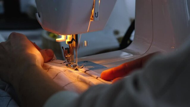 Sewing process on a sewing machine, a needle with a thread and a holder close-up stitch the white checkered fabric.