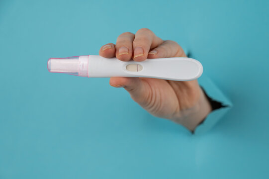 A hand with a negative pregnancy test sticking out of a hole in a blue cardboard background. 