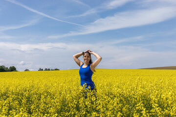 woman portrait and flowers, a dark hair woman  in a blue dress is smelling on a canola flower in...