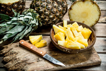 Pieces of fragrant pineapple in a bowl on a cutting Board with a knife.