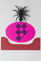 paper spider glyph or dingbat cutout at the edge of a pink paper oval with checkered pattern and...