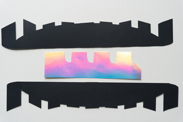 two paper stripes with cut edges and iridescent cut paper object on blank paper