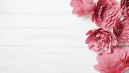 白い木目の背景にピンク色の紙で作られた複数の花。春の背景イメージ。俯瞰。（横長）