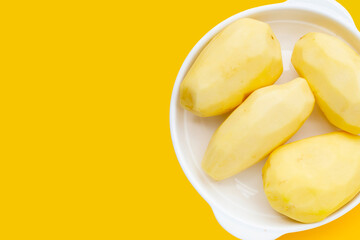 Raw peeled potatoes in white plate on yellow background.
