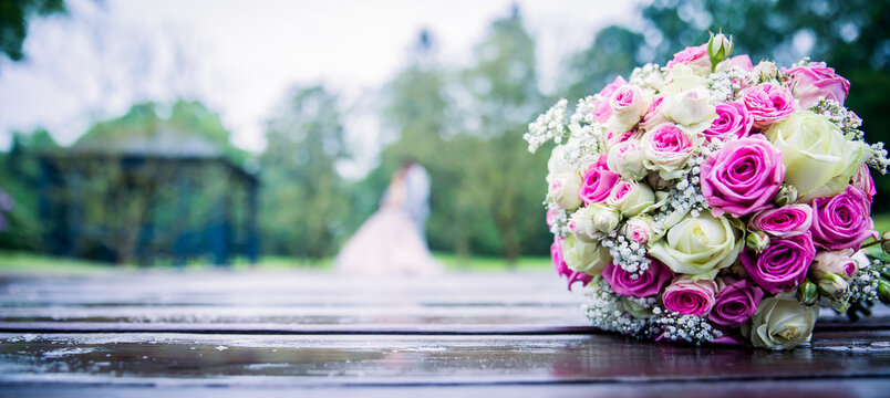 bridal bouquet of mix flowers on a field with a couple in the background bokeh, room for text header image