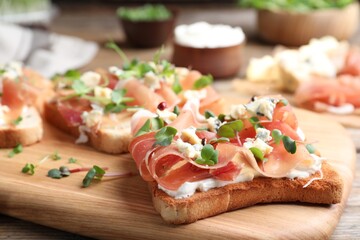 Delicious sandwiches with prosciutto, cheese and microgreens on wooden table, closeup