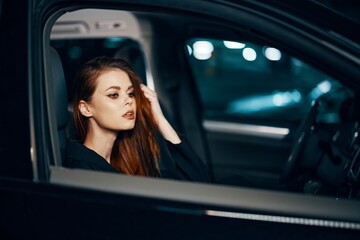 Fototapeta na wymiar a stylish, luxurious woman sits in a black car at night, touching her face with a thoughtful expression. Close horizontal photo