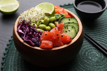 Delicious poke bowl with vegetables, fish and edamame beans on black table, closeup