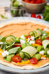 Tortilla with hummus and vegetables on table, closeup
