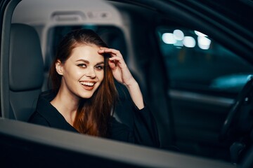a stylish, luxurious woman sits in a black car at night in the passenger seat, and looks pleasantly into the camera. Close horizontal photo