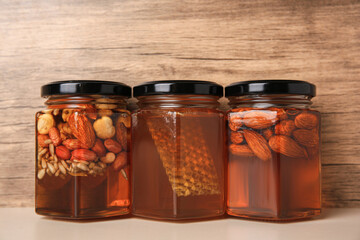 Jars with different nuts and honey on light table near wooden wall