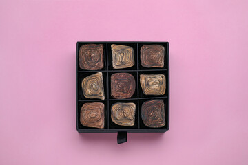 Box of tasty chocolate candies on pink background, top view