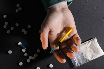 Addicted man with syringe near drugs at black textured table, top view