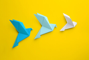 Origami art. Colorful handmade paper birds on yellow background, flat lay