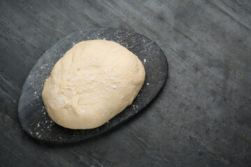 Fresh yeast dough with flour on black table, top view. Space for text