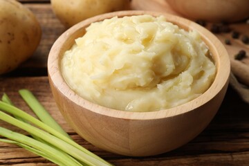 Bowl of tasty mashed potato, pepper and leeks on wooden table, closeup