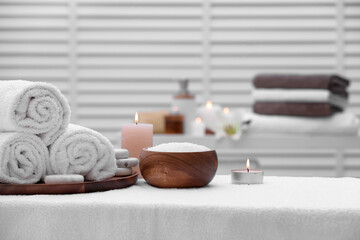 Spa composition with rolled towels and burning candles on massage table in wellness center, space for text