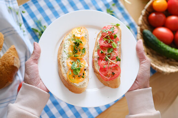 Aged woman holds in her hands a plate with healthy sandwiches with microgreens and vegetables
