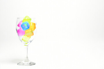 Cubos de colores dentro de una copa de vidrio, aislados en un fondo blanco. Espacio para texto al lado derecho.