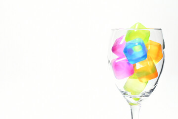 Cubos de colores dentro de una copa de vidrio, aislados en un fondo blanco. Espacio para texto al lado izquierdo.