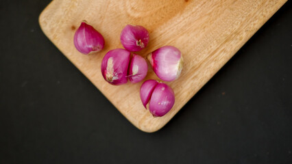 Peeled shallots on wooden cutting board, healthy vegetables and medicine. Isolated on black background.