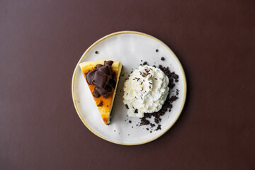 chocolate brownie cheesecake with whipped cream on white dish or plate and brown table by top view for sweet dessert or snack and food in bakery coffee shop or cafe restaurant