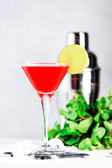 Cosmopolitan classic alcoholic cocktail with vodka, liqueur, cranberry juice, lime, ice. Gray table background, bar tools, copy space