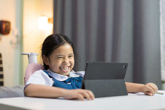 Asian Child Smile Learning On Computer Tablet Or Kid Girl Student Laughing Fun To Studying Online Class Or Person Wear School Uniform Happy Learn From Home And Back To School By Video Call Education