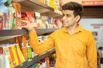 Young Indian man buying at grocery shop or supermarket. Asian male choose snacks and food shopping at store.