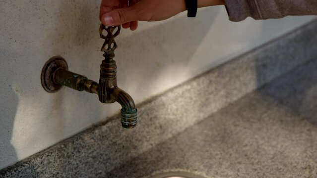 man hand close flowing water from faucet and stops senseless consumption and waste of water to nowhere. Caring for environment. Closing tap with running cold water in nature.