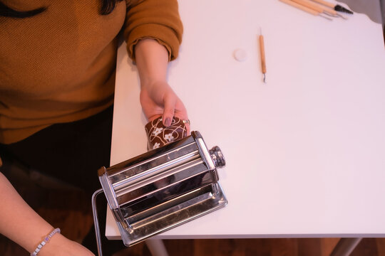 Woman using the pasta machine to flatten the clay