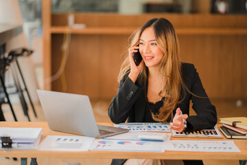 Asian businesswoman working on charts and graphs showing results in office with documents and laptop Worker documents calculating financial indicators, smiling and happy with success.