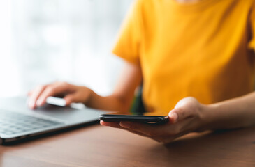 Hand holding smartphone and using laptop.