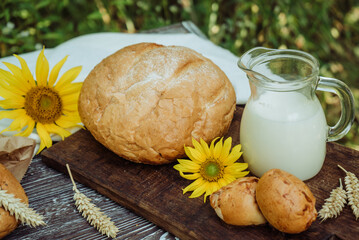 homemade wheat bread, freshly buns, mug with farm milk, sunflower, baked goods on brown wooden...