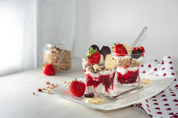 Strawberry valentine's day dessert decorated with heart-shaped chocolate and ripe berries Two glasses with a sweet breakfast of cream cheese and pureed berries on a white wooden table. Side view.
