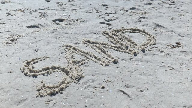 Sand written on beach in capitals with a finger in 
white sand Slow Pan