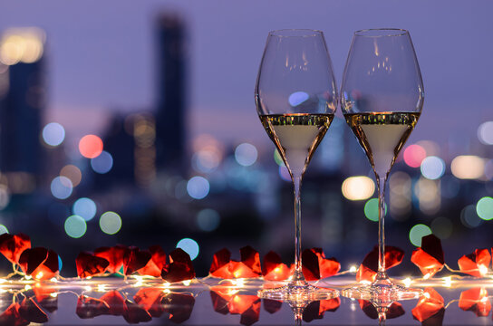 Two glasses of white wine on table with light and heart papar fold with colorful bokeh light from city background for Valentines dining concept.