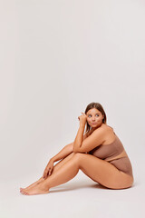 Fototapeta na wymiar Plus size self enjoyed woman wearing lingerie sitting on a floor isolated over white background 