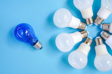 Top view of white light bulb in round shape with one blue light bulb on light blue background ,...