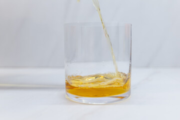 Pouring whiskey in a wide whiskey glass on kitchen surface with bright background