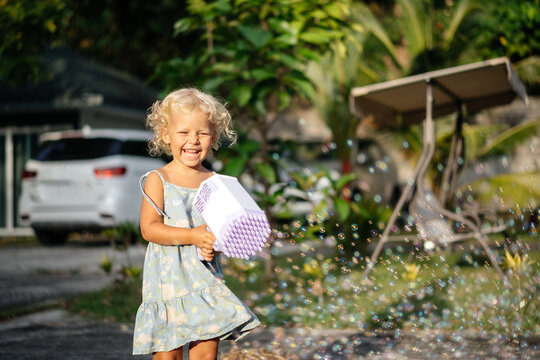 Portrait of a child of a curly blonde girl Blowing soap bubbles from a gun in summer. Playing outside on a sunny summer day.