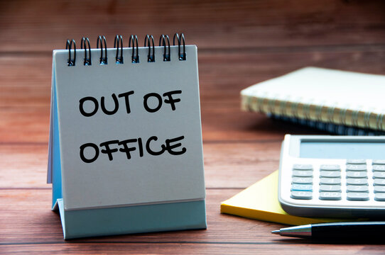 Out of office text on calendar desk with notebook, calculator and pen background. Out of office concept.