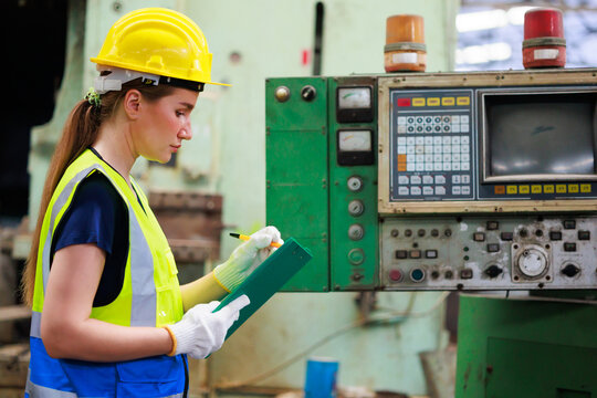 caucasian female engineering worker wearing safety hardhat helmet inspecting auto robot lathe machine to drill components. Metal lathe industrial manufacturing factory