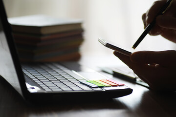 Hands using laptop and phone for online shopping, close up clean image in front of the window in soft light