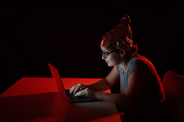 Paranoid caucasian woman typing on a computer wearing a tinfoil cap. Conspiracy theory.